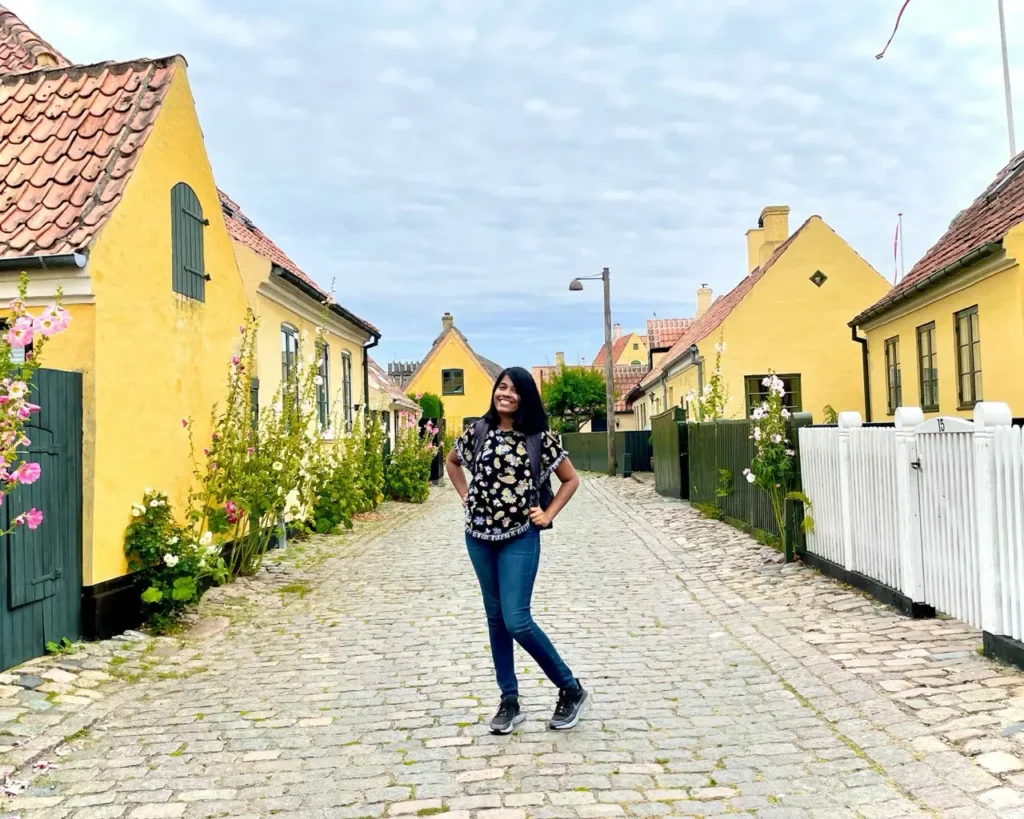 Agalya standing among the colored houses of Dragor Gamle By (Old Town)